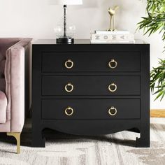 a pink chair sitting next to a black chest of drawers in a room with white walls