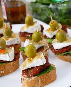 mini sandwiches with olives, cheese and meat on them sitting on a white plate