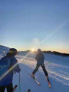 two people on skis in the snow at sunset