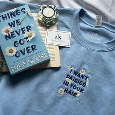 a blue t - shirt with white daisies on it next to a book and candle