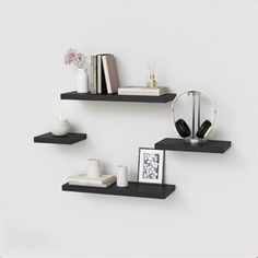 three black floating shelves with books and headphones on each shelf in front of a white wall