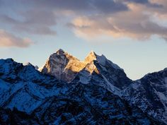 the mountains are covered in snow as the sun is low to the ground and dark clouds can be seen above them