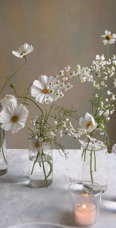 three vases filled with white flowers sitting on top of a table next to a candle