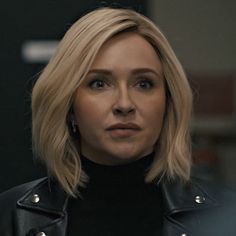 a woman with blonde hair wearing a black turtle neck sweater and leather jacket looking at the camera