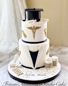 a three tiered cake is decorated with gold and white medical symbols, including a doctor's stethoscope