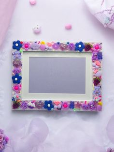 a white frame decorated with colorful buttons and flowers on a pink surface surrounded by other items