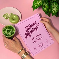 two hands holding a pink menu next to a green donut on a white plate