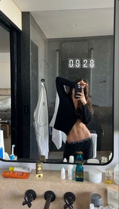 a woman taking a selfie in front of a bathroom mirror with her hair combed