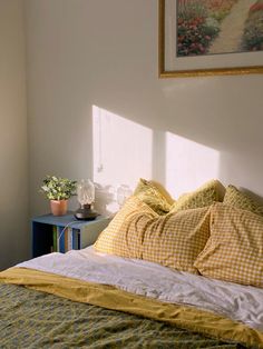 a bed with yellow and white sheets in a bedroom next to a painting on the wall