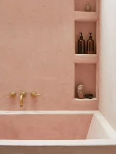 a bathtub with pink walls and gold faucets in the corner is shown