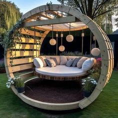 a circular couch sitting in the middle of a lush green yard with hanging lights and lanterns