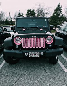 a jeep with pink lights parked in a parking lot next to other cars and trees