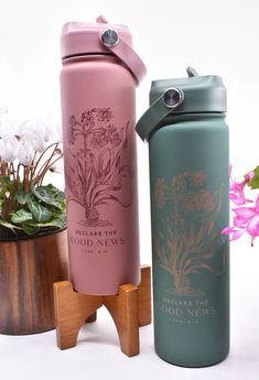 two water bottles sitting next to each other in front of some potted plants and flowers