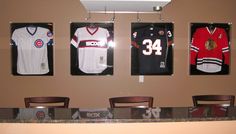 three framed hockey jerseys hang on the wall above a table with four chairs in front of them