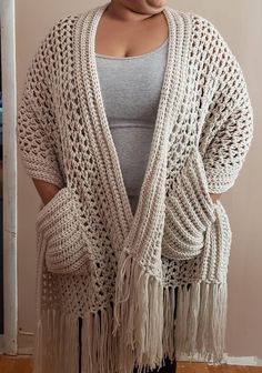 a woman standing in front of a wall wearing a white knitted cardigan