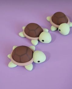 three plastic turtle figurines sitting on top of a purple surface with white and brown trim