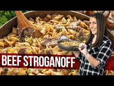 a woman holding a skillet full of food in front of a pile of pasta