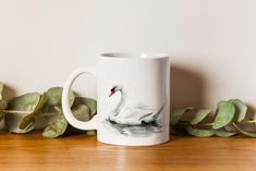 a white swan mug sitting on top of a wooden table next to some green leaves