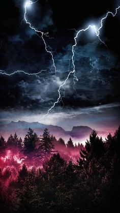 the sky is full of lightning and clouds above some trees in the foreground, with mountains in the background