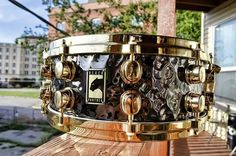 a close up of a metal drum on a wooden surface near a building and trees