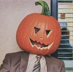 a man wearing a suit and tie with a pumpkin on his head in front of him