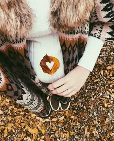 a woman is holding a leaf in her hands and wearing a sweater with a heart on it