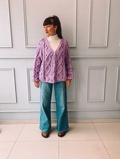 a woman standing in front of a wall wearing a purple sweater and wide legged jeans