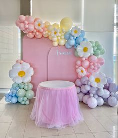 balloons and flowers decorate the backdrop for a baby's first birthday party in pastel colors