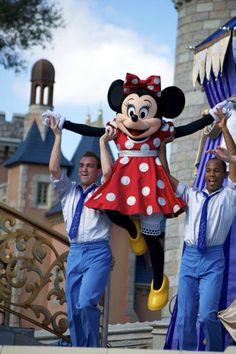 some people are dressed up and dancing in front of a castle with minnie mouse on it