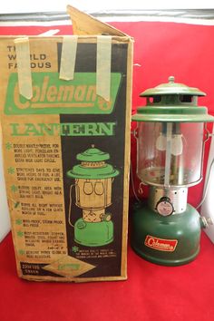 an old style lantern sitting on top of a red cloth covered table next to a cardboard box