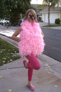 a woman in pink is standing on the sidewalk with her legs crossed and wearing a pink feathered vest