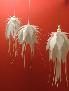 three white paper flowers hanging from strings against a red wall