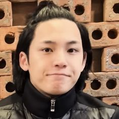 a man with long hair standing in front of stacks of bricks and wearing a black jacket