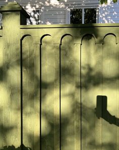 the shadow of a person holding a cell phone in front of a wooden fence with a white house behind it