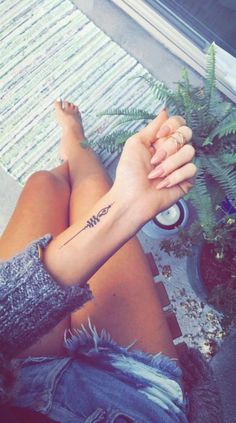 a woman's arm with a small tattoo on her left wrist, sitting next to a potted plant