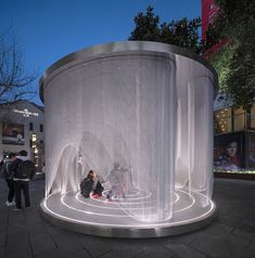 two people sitting on the ground in front of a circular structure with sheer fabric covering it