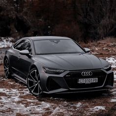 the front end of a grey car parked on snow covered ground with trees in the background