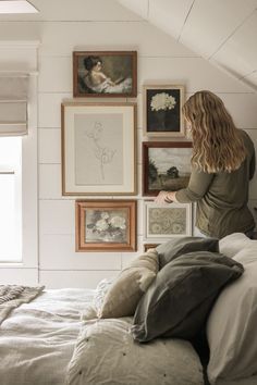 a woman standing on top of a bed in a bedroom next to pictures and paintings