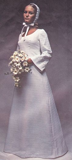 a woman in a white dress holding a bouquet of flowers and wearing a head scarf