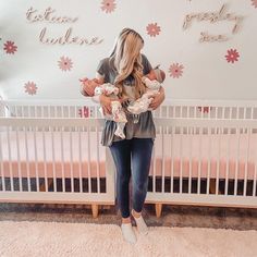 a woman standing in front of a wall with flowers on it holding two baby's