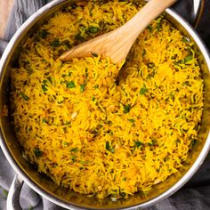 a pot filled with yellow rice on top of a gray table cloth and wooden spoon