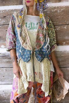 a woman standing next to a wooden wall with flowers in her hair and an open jacket over her shoulders