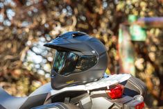 the helmet is sitting on the motorcycle's back end and there are trees in the background