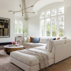 a living room with white furniture and large windows on the wall, along with an ottoman