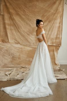 a woman standing in front of a backdrop wearing a white wedding dress with an open back