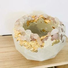 a white vase with gold leaf decoration on top of a wooden table next to a wall