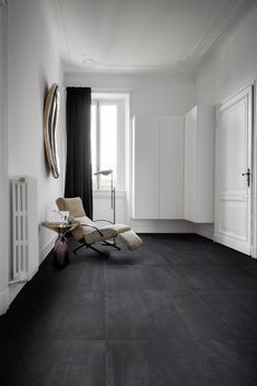 an empty room with black and white floors, a large window, and a chaise lounge chair