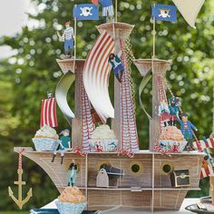 a table topped with cupcakes and an old fashioned pirate ship cake topper