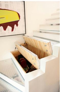 an open drawer on the side of a white wall in front of a painting and stairs