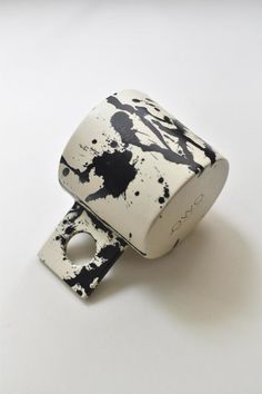 a black and white object with paint splattered on it's side, sitting on a table